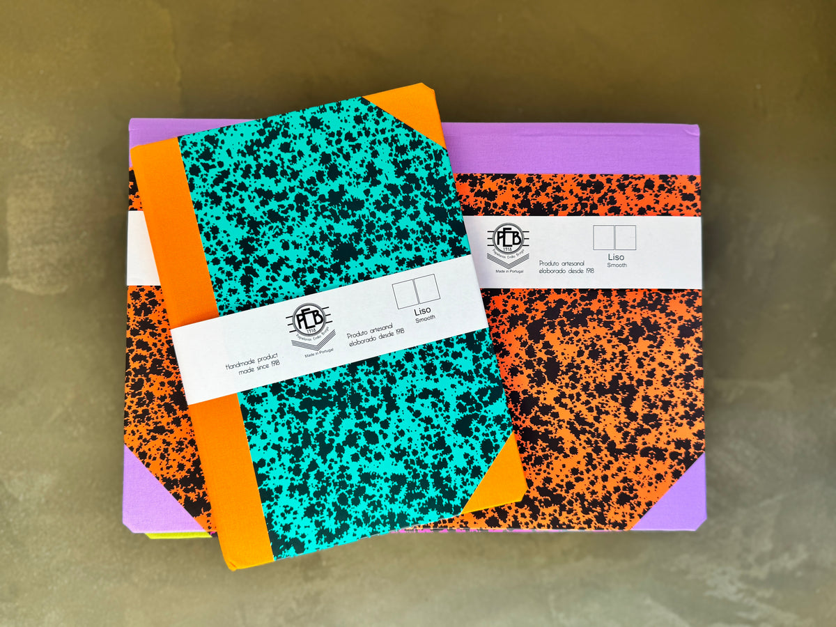 Three colorful composition notebooks stacked on top of each other, featuring black and teal, black and orange, and black and purple covers with white paper bands across the middle.