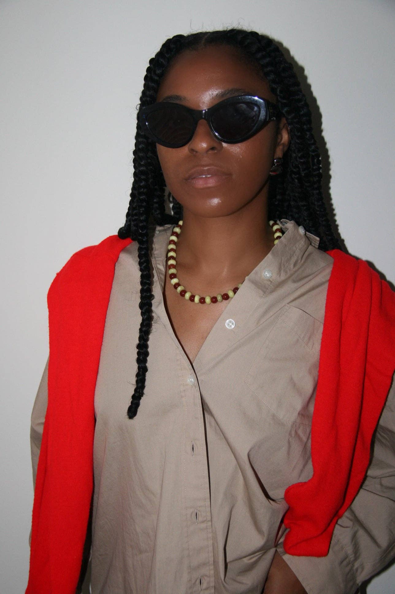 Person wearing sunglasses, beige shirt, and red jacket against a plain background