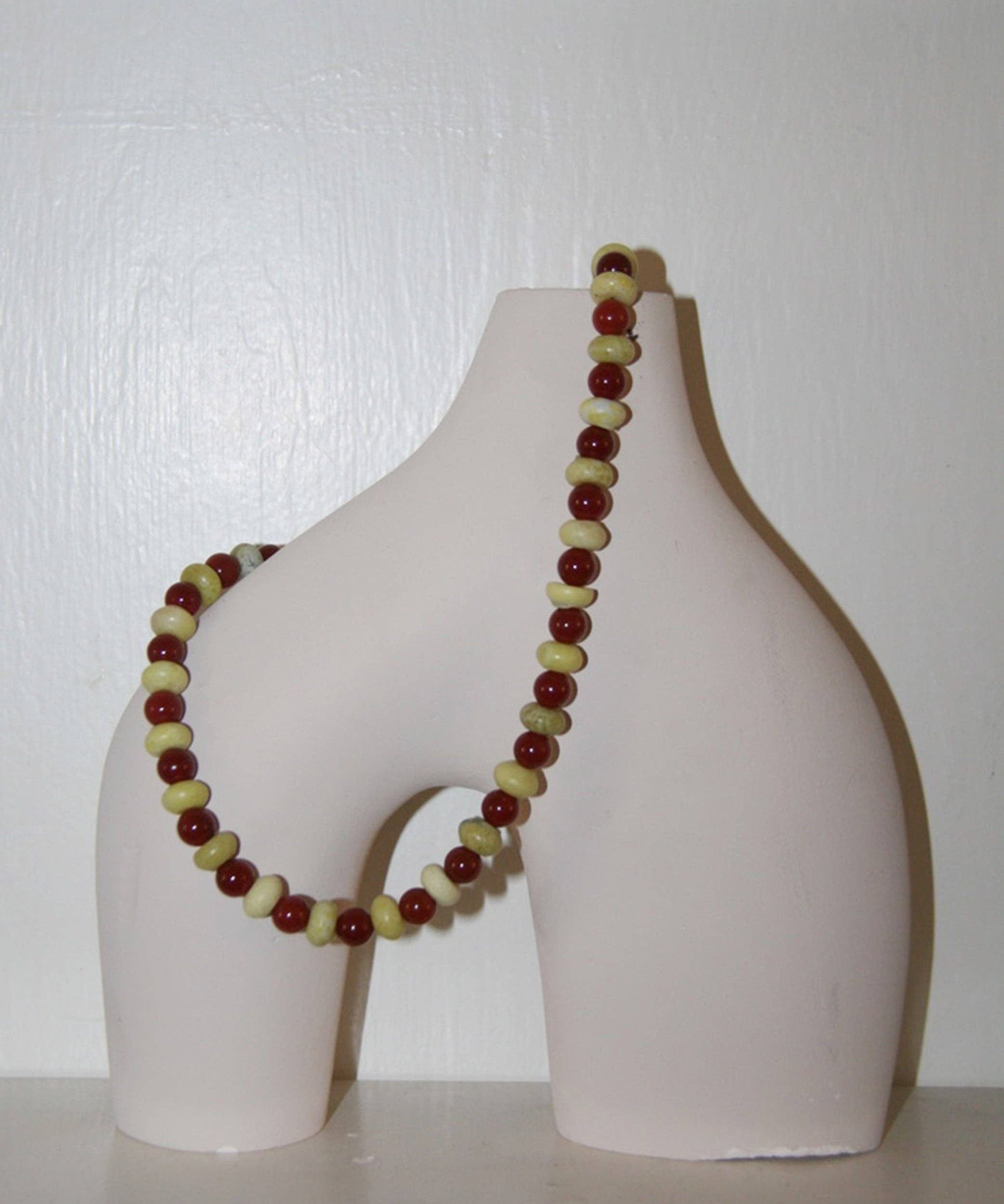 Beaded necklace on a white ceramic vase against a white background