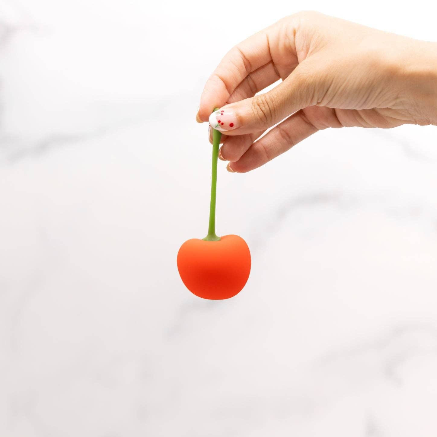 Hand holding a small red cherry against a white background