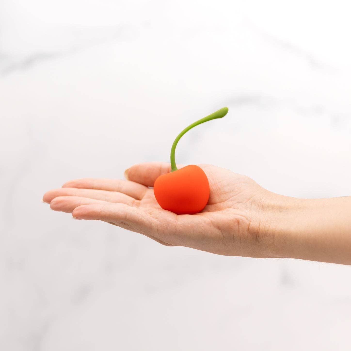 Hand holding a red fruit-shaped object with a green stem on a white background