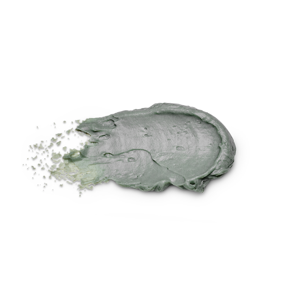 A thick, textured smear of sage green cosmetic cream or clay mask on a solid white background, with fine particles visibly splashing from the left side.