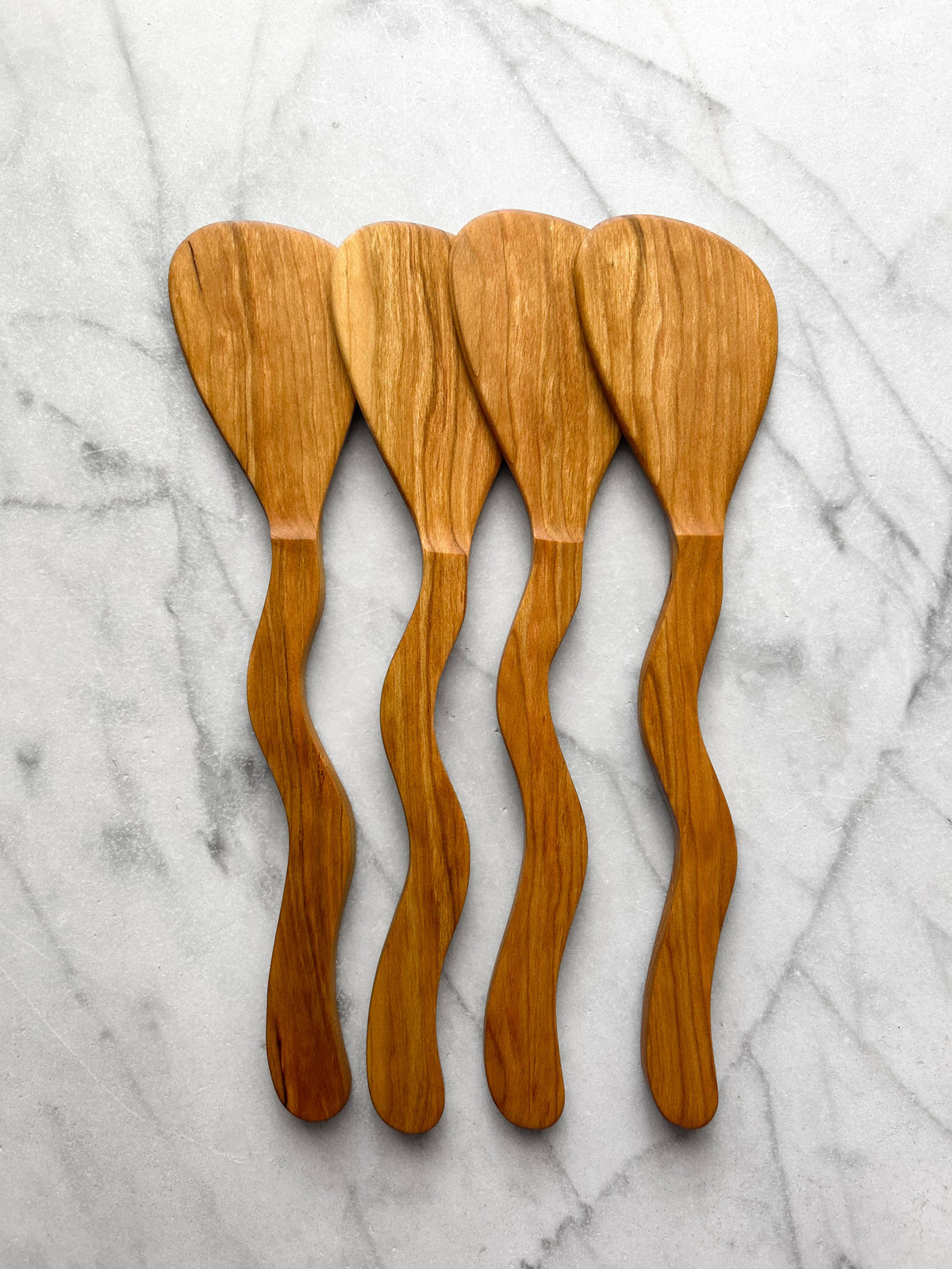 Four wooden spoons with wavy handles on a marble surface