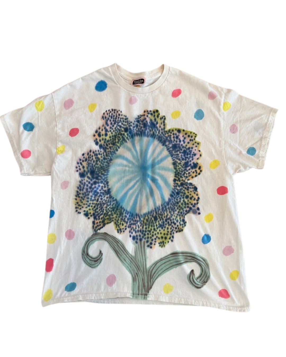 A white short-sleeve t-shirt featuring a large, colorful graphic of a flower with blue, green, and yellow tones, decorated with scattered multicolored polka dots.
