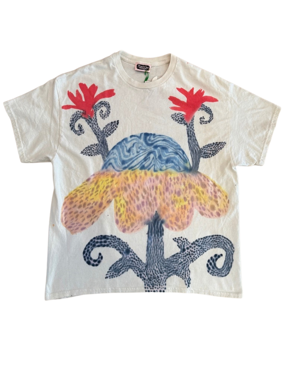 A cream-colored short-sleeve t-shirt featuring a colorful graphic print of a stylized flower with red petals, a blue marbled center, and a yellow-orange spotted lower section, all framed by dark blue dotted scrollwork.