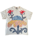 A cream-colored short-sleeve t-shirt featuring a colorful graphic print of a stylized flower with red petals, a blue marbled center, and a yellow-orange spotted lower section, all framed by dark blue dotted scrollwork.
