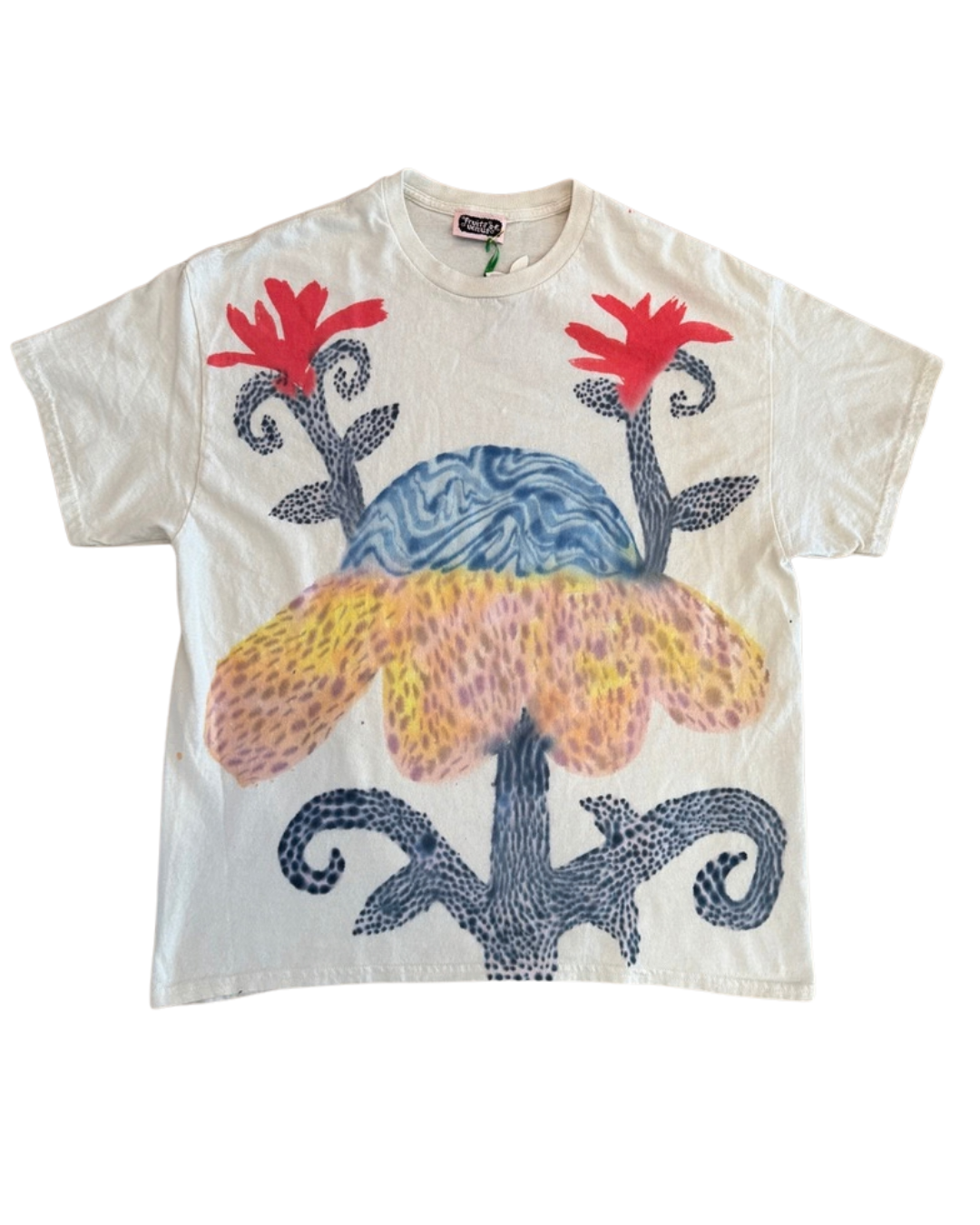 A cream-colored short-sleeve t-shirt featuring a colorful graphic print of a stylized flower with red petals, a blue marbled center, and a yellow-orange spotted lower section, all framed by dark blue dotted scrollwork.