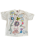 A white short-sleeve t-shirt featuring a colorful retro graphic print of flowers, a butterfly, and abstract shapes, laid flat against a white background.
