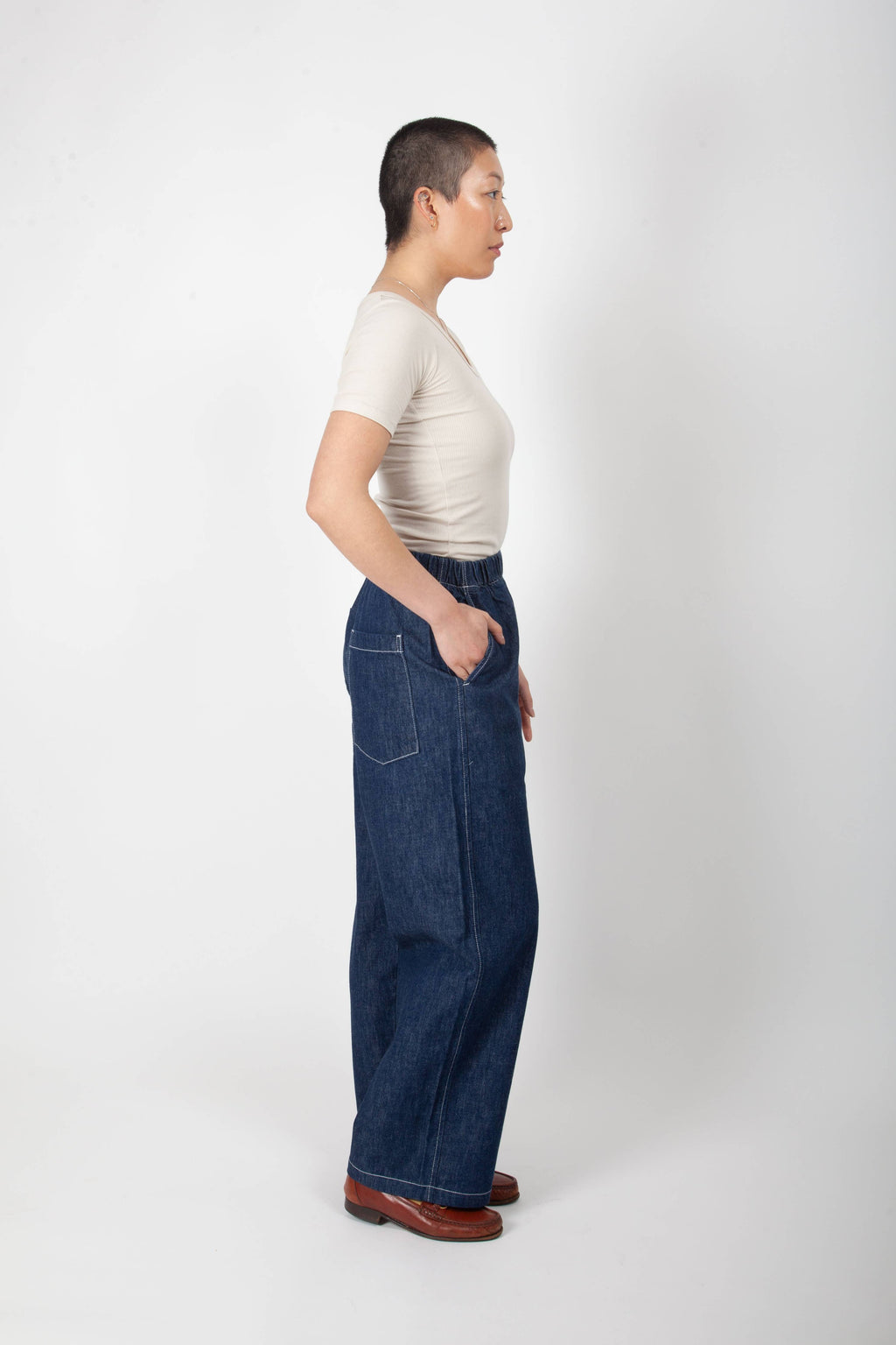 Person wearing a beige top and blue jeans standing against a white background
