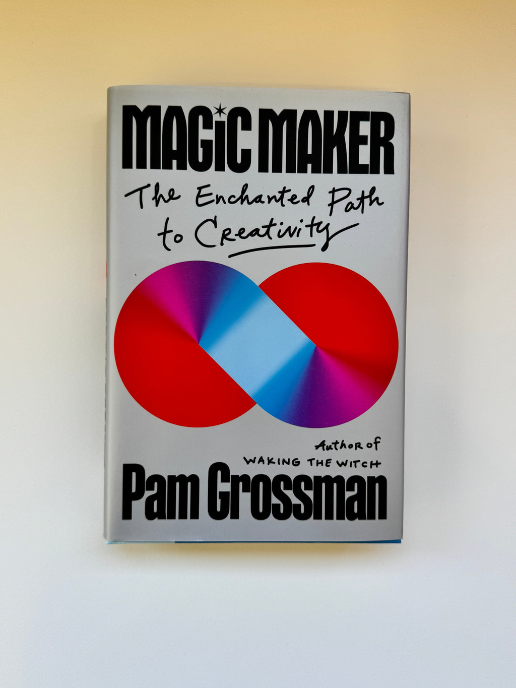 The book 'The Enchanted Path to Creativity' by Pam Grossman, featuring a silver-gray cover with a large red and purple infinity symbol containing a light blue center, photographed on a light beige background.
