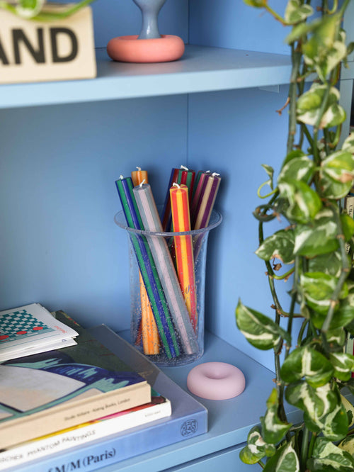 Colorful pencils in a clear cup on a blue shelf with books and decorative items.