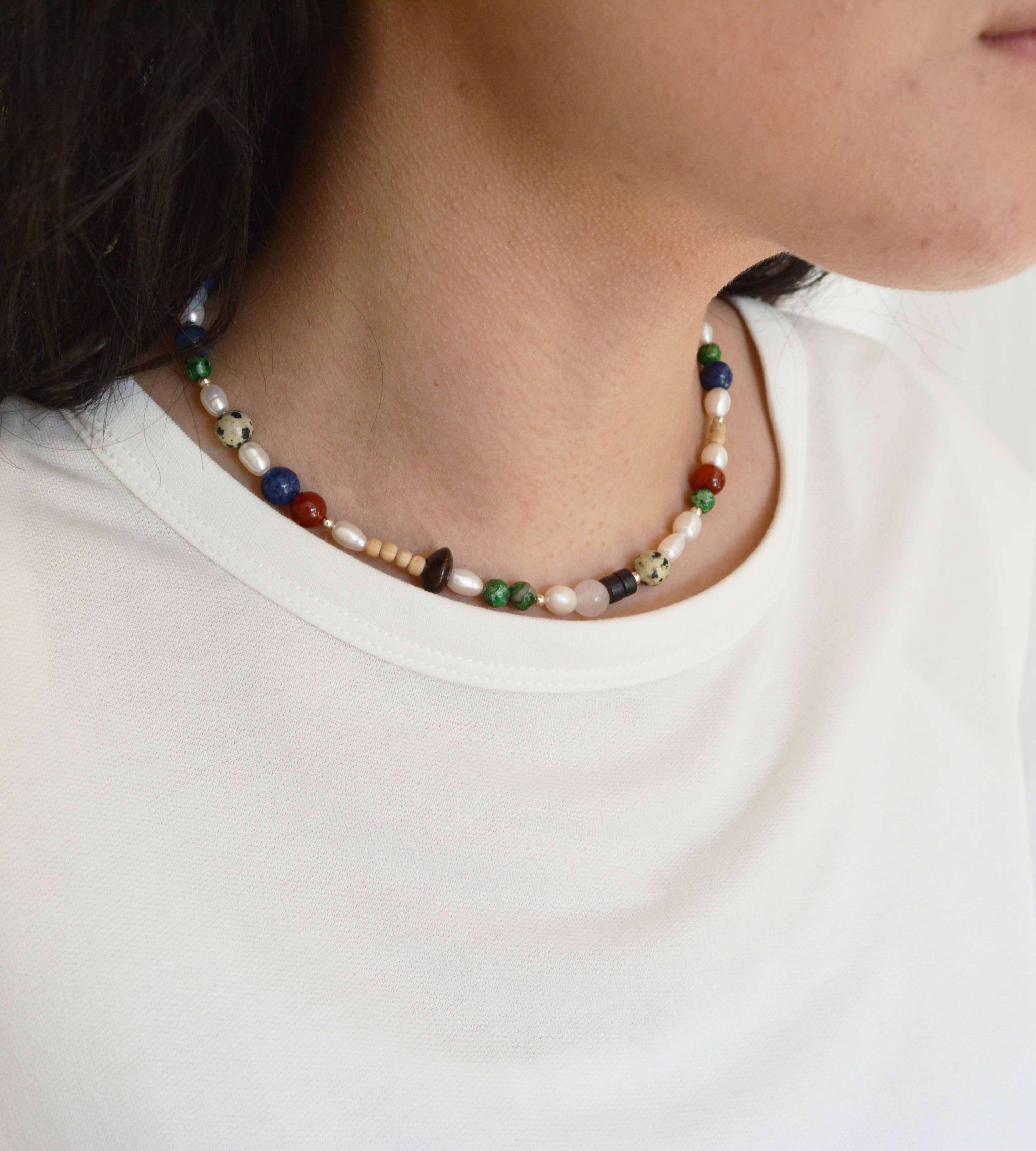 Person wearing a beaded necklace with a plain white shirt