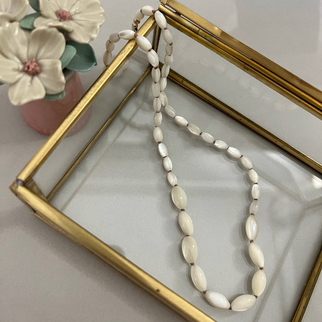 Necklace with white beads on a gold-framed mirror with flowers in the background