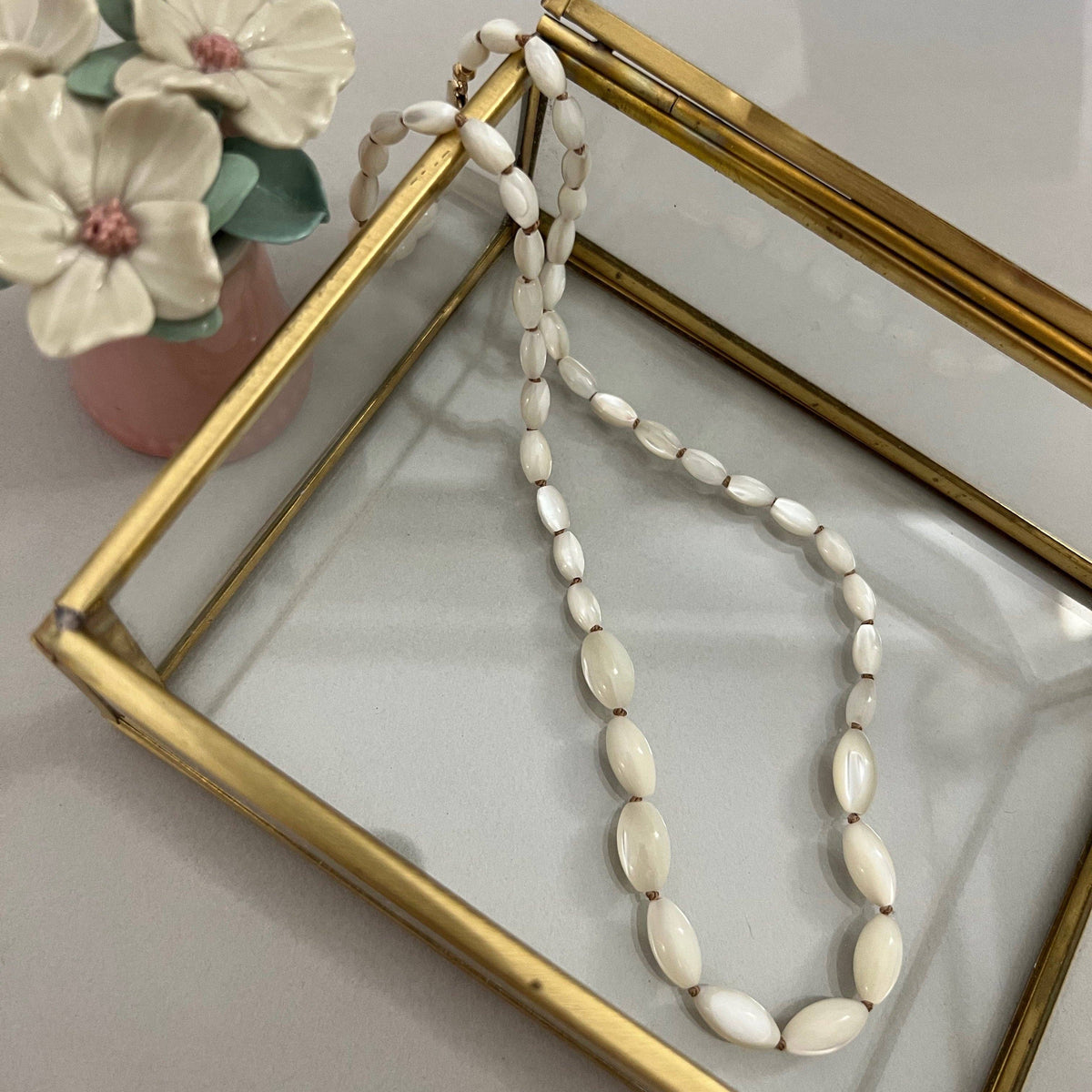 Necklace with white beads on a gold-framed mirror with flowers in the background