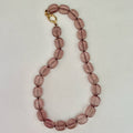 Necklace with purple beads and a gold clasp on a light gray background