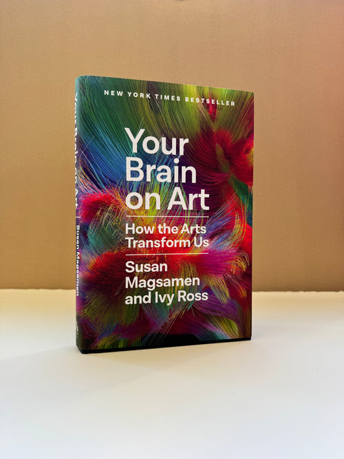 The book 'Your Brain on Art' by Susan Magsamen and Ivy Ross, standing upright on a white surface against a beige background. The cover features a vibrant, multicolored abstract design resembling paint or light streaks.